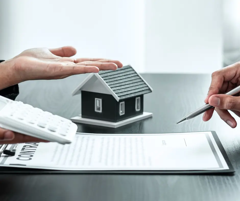 a person's hands holding a calculator, a house and a contract on a table