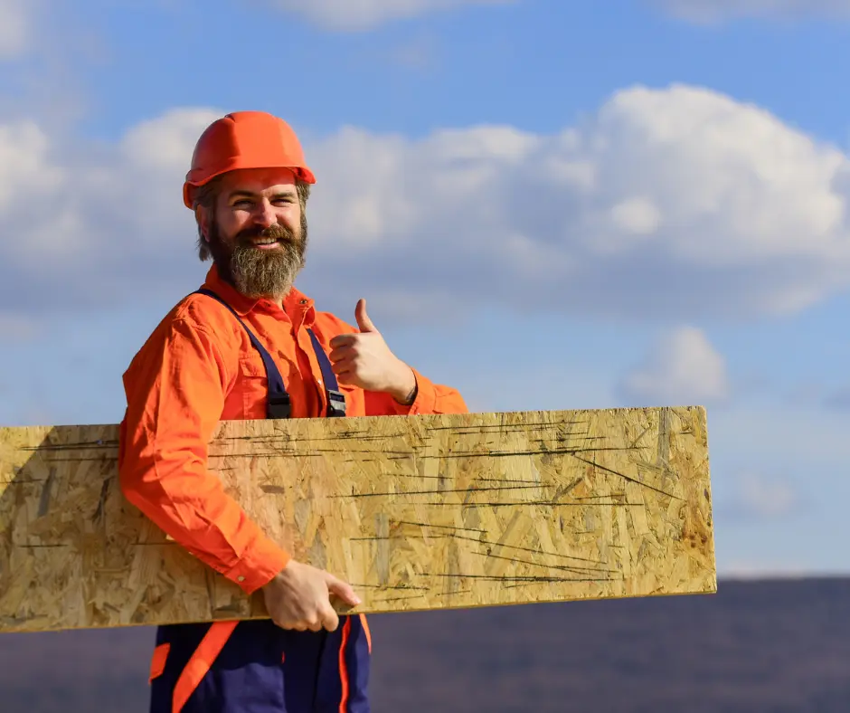 a man in orange hard hat holding a wooden board on a roof