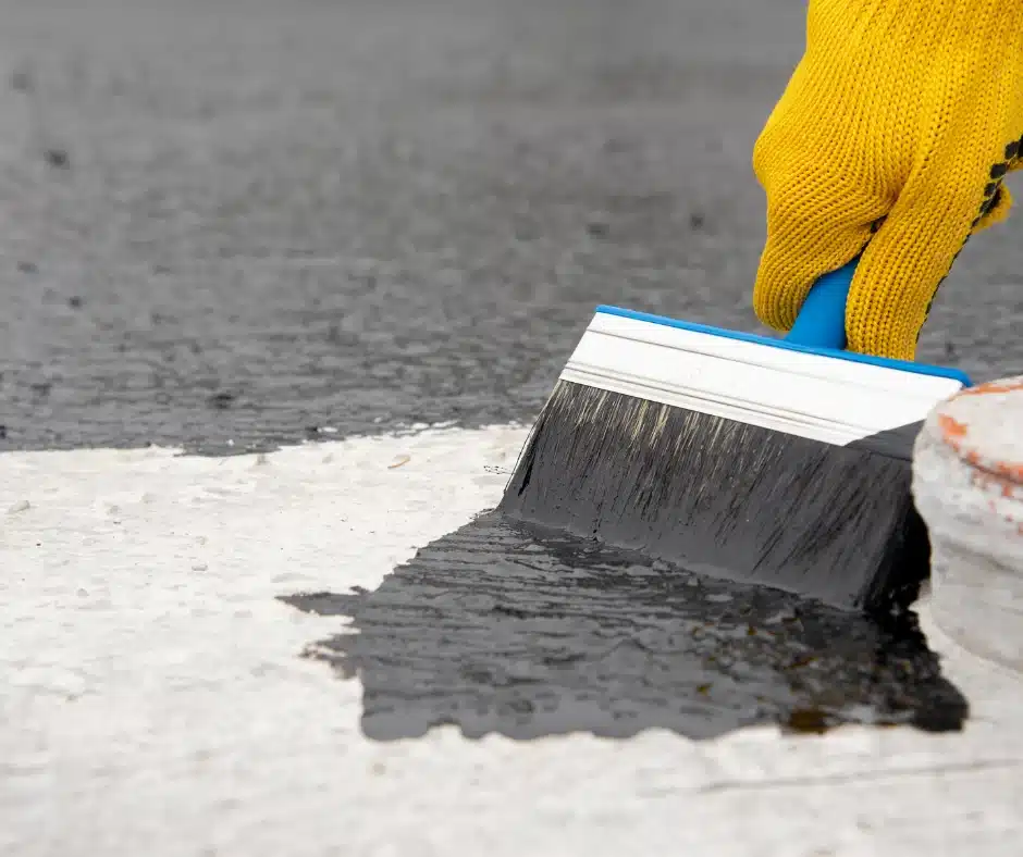 a person using a brush to apply roof coating