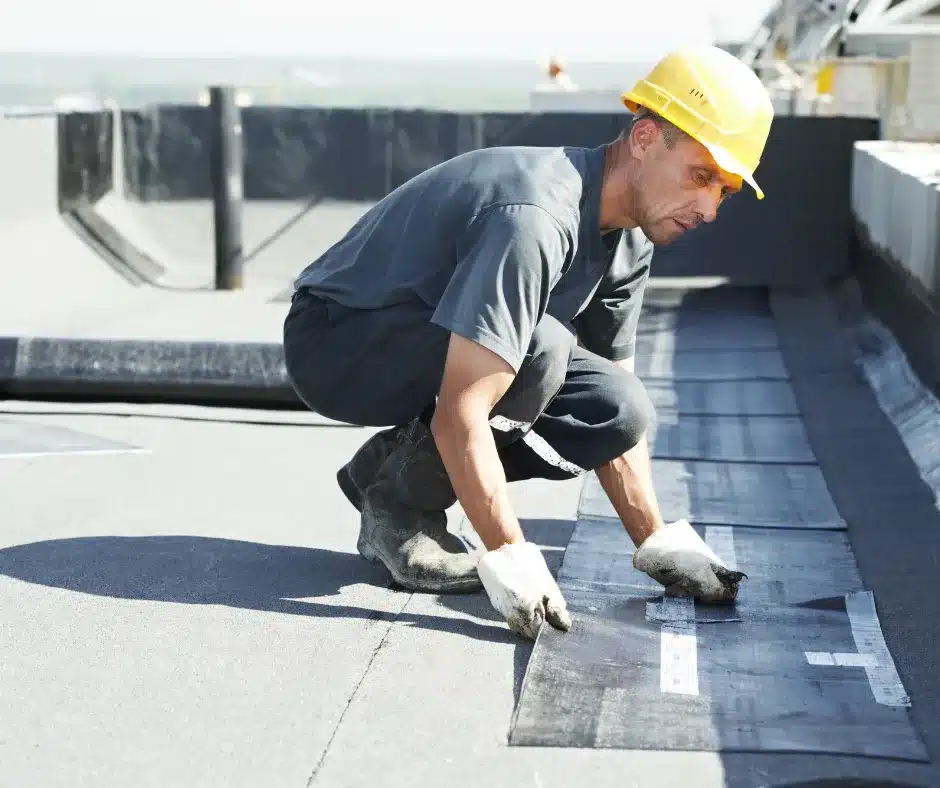 a man wearing a hard hat and gloves bending over on a roof