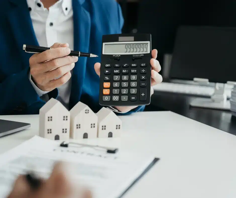 a person holding a calculator and pen, miniature houses in front of him